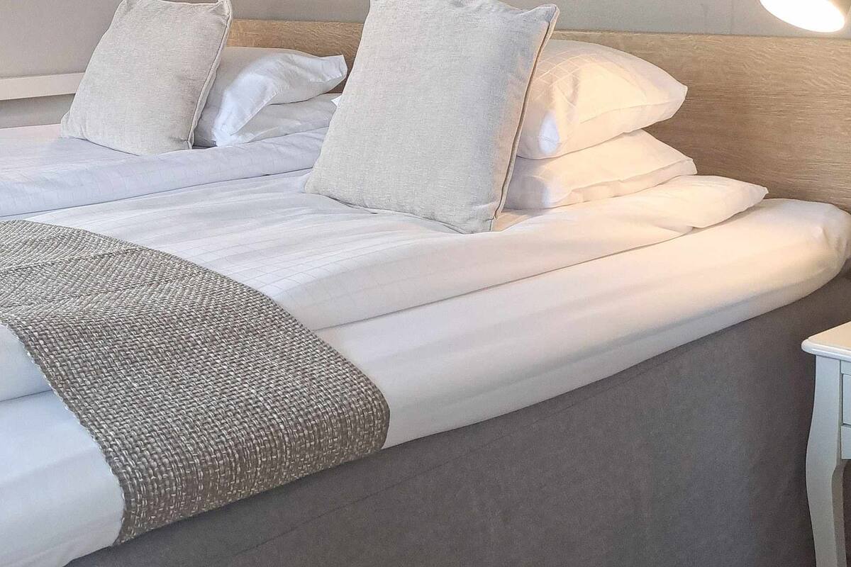 A neatly made bed with white linens and pillows, two bedside lamps, and a framed picture on the wall.