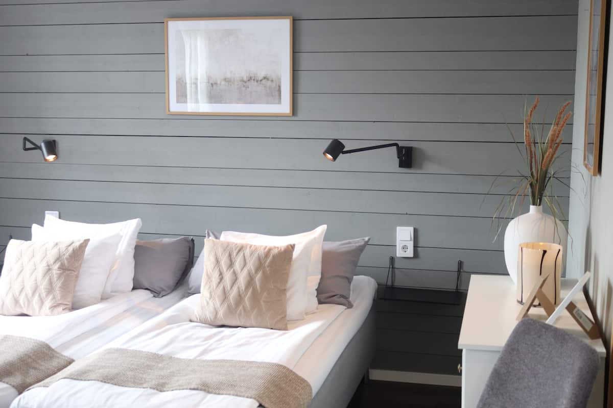 A modern bedroom with a bed, bedside lamps, a framed artwork, and a vase with plants.