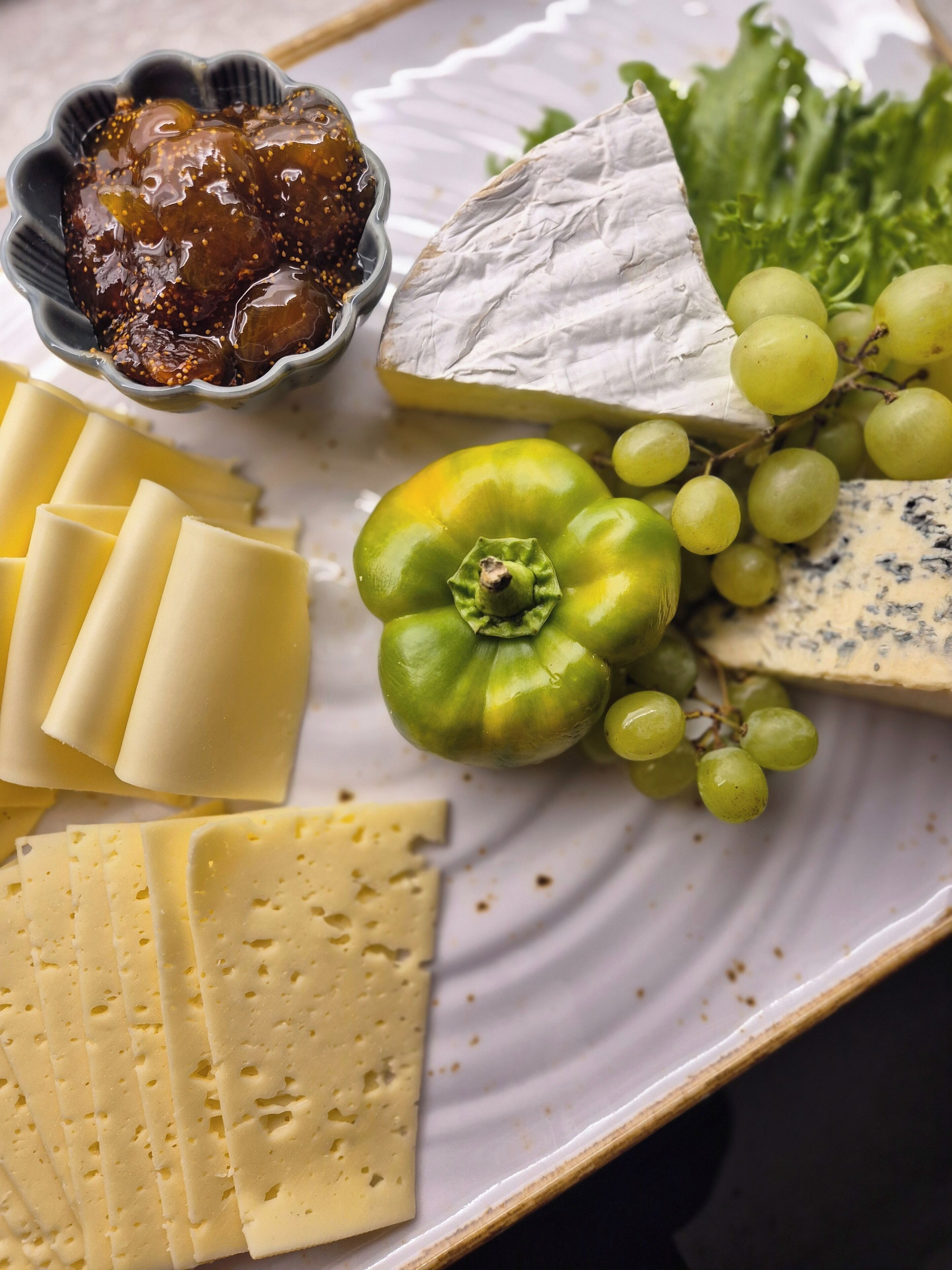 A variety of cheeses, grapes, and a bowl of chutney on a plate.
