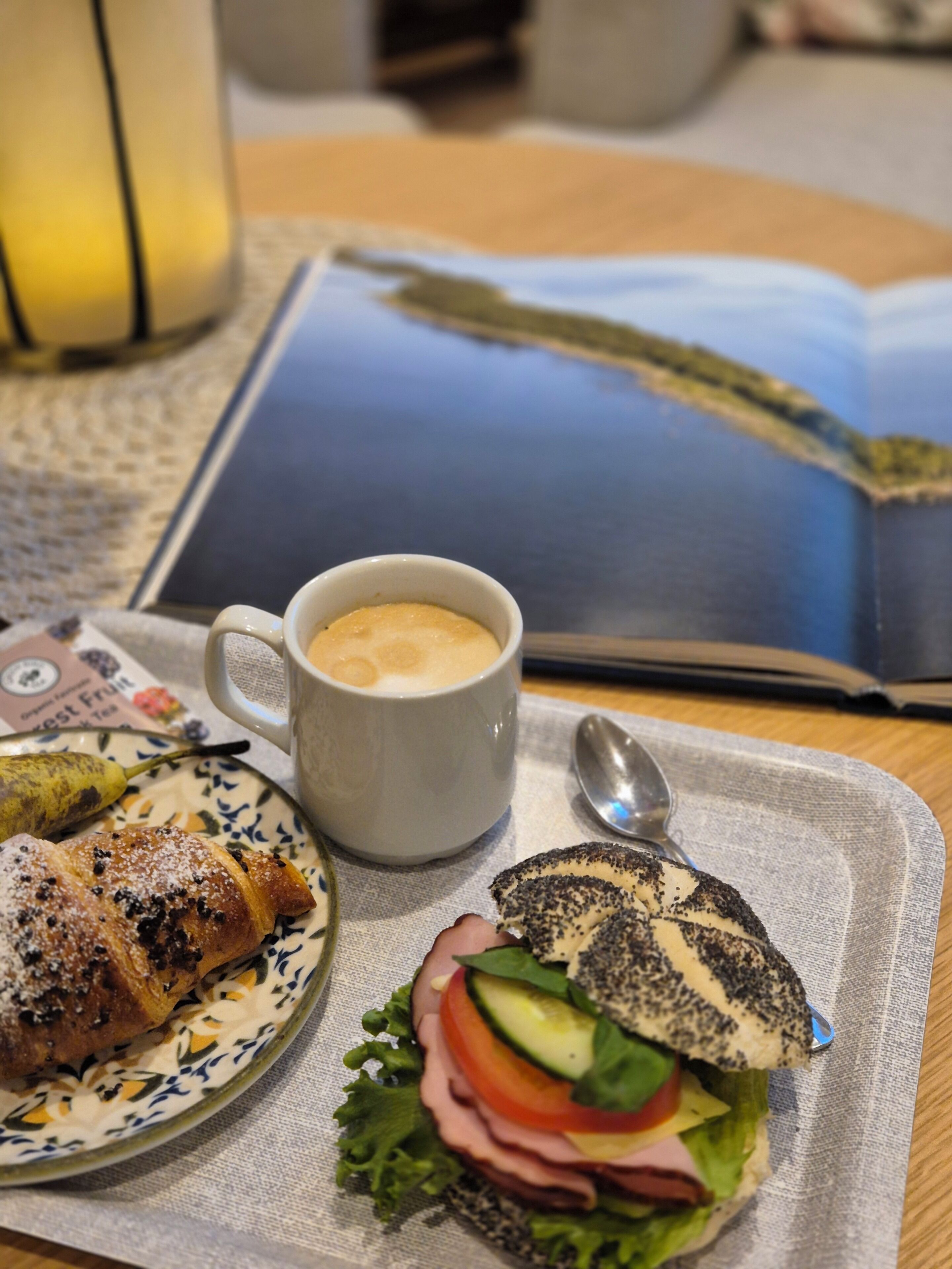 Ein Tablett mit einem Sandwich, einer Kaffeetasse und einem Buch auf einem Tisch.