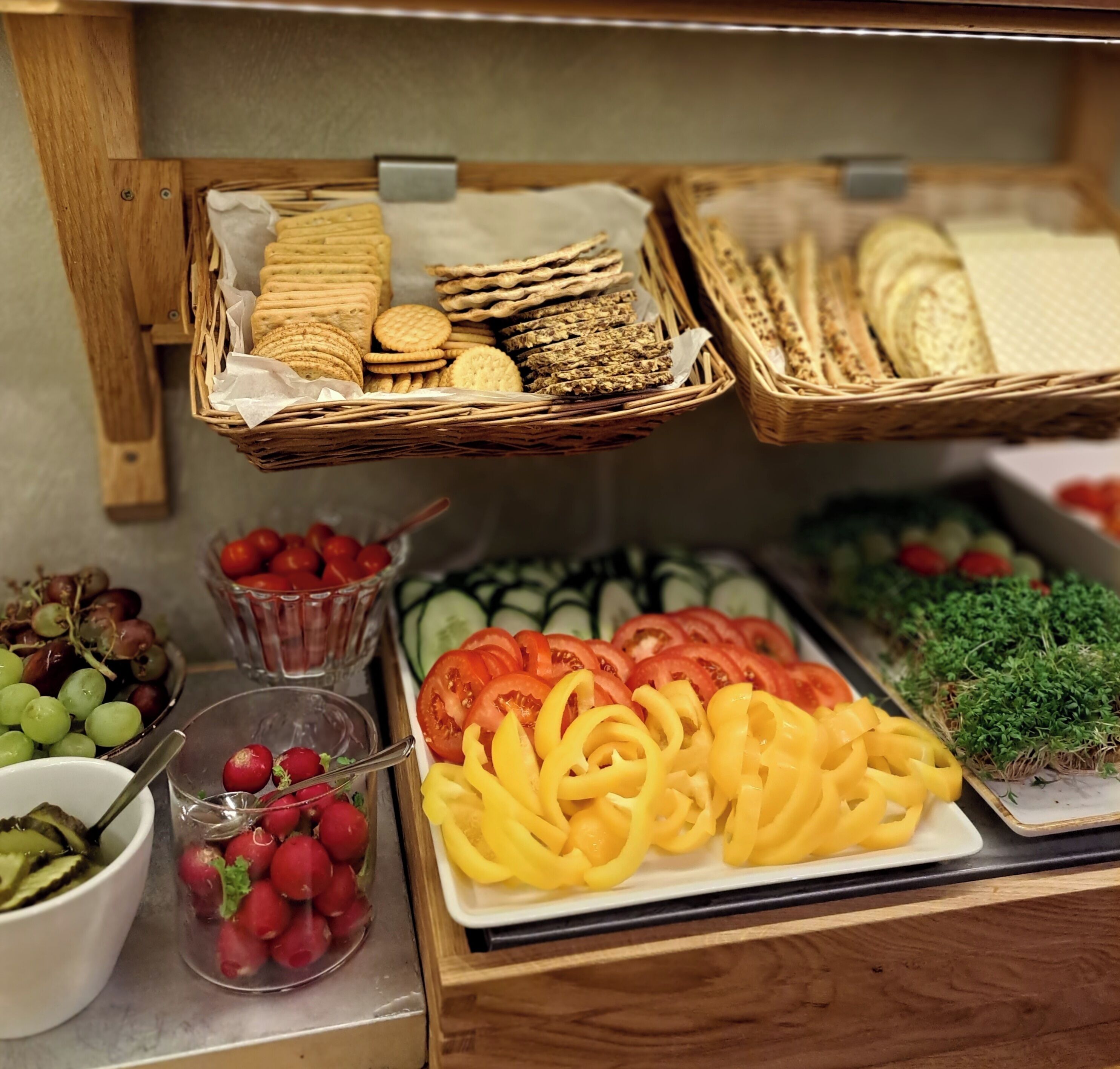 En buffet med forskellige spiser, herunder kiks, skiveskåret brød og friske grøntsager som tomater og agurker.