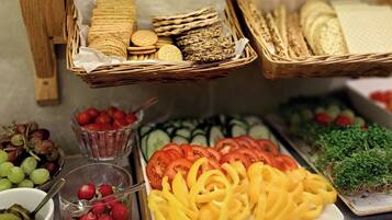 En buffet med forskellige spiser, herunder kiks, skiveskåret brød og friske grøntsager som tomater og agurker.
