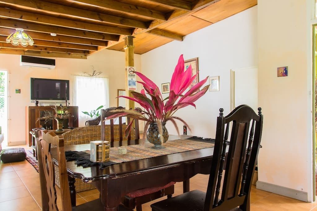 Uma área de refeições com mesa de madeira, cadeiras e um vaso com flores cor-de-rosa.