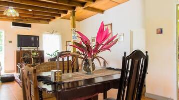 Uma área de refeições com mesa de madeira, cadeiras e um vaso com flores cor-de-rosa.