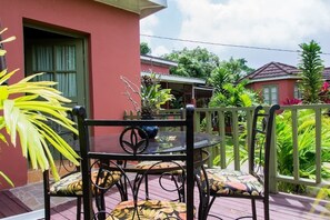 A patio with a round table and chairs, surrounded by a wooden fence and lush greenery. - The Grand Sinopia Inn Portland (Port Antonio)