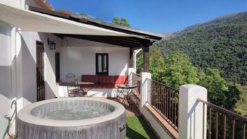 A balcony with a hot tub, seating area, and a scenic mountain view.