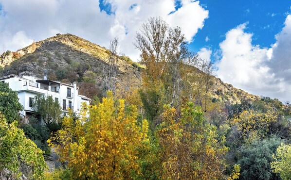 A white building with balconies, surrounded by autumn foliage and a mountain backdrop. - Casa Rural Arroyo de la Greda (Guejar Sierra)