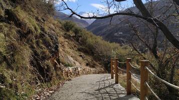 A paved path with wooden posts and ropes, surrounded by dry vegetation and mountains in the background.