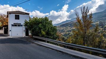 A rural house named "Casa Rural" with a white exterior and a tiled roof, located at the base of a road with a metal guardrail.