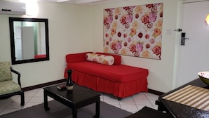 Ein Wohnzimmer mit einem roten Sofa, einem gemusterten Sessel, einem schwarzen Couchtisch und einem an der Wand befestigten Spiegel.