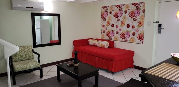 A living room with a red sofa, a patterned armchair, a black coffee table, and a wall-mounted mirror.