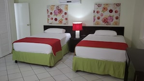 Ein Zimmer mit zwei Betten, jeweils mit einer grünen Tagesdecke und weißen Kissen, einer roten Nachttischlampe sowie floralen Bildern an den Wänden.