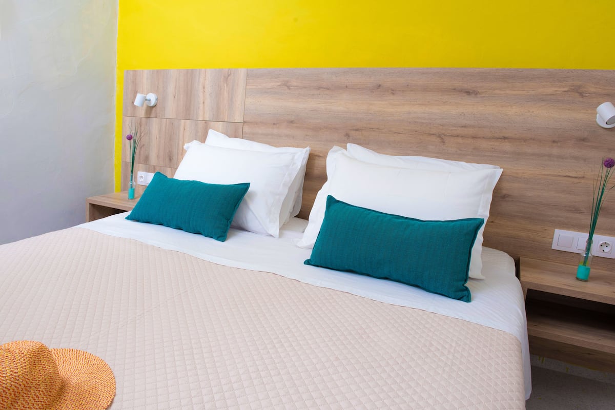 A bed with white and teal pillows, a quilted beige bedspread, and wooden headboard.