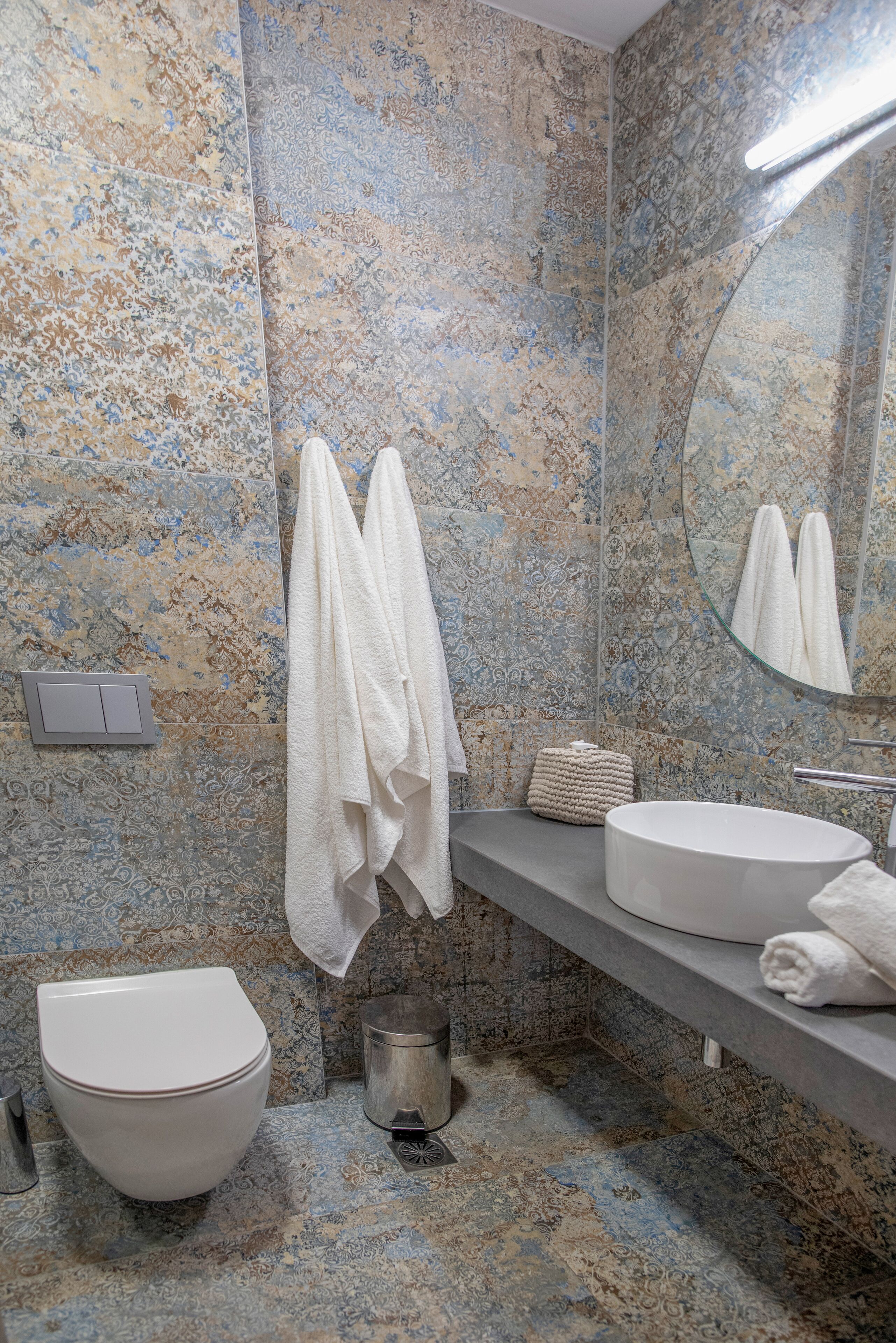 Un baño con pared con diseño de mármol, un inodoro, un lavabo y un espejo.