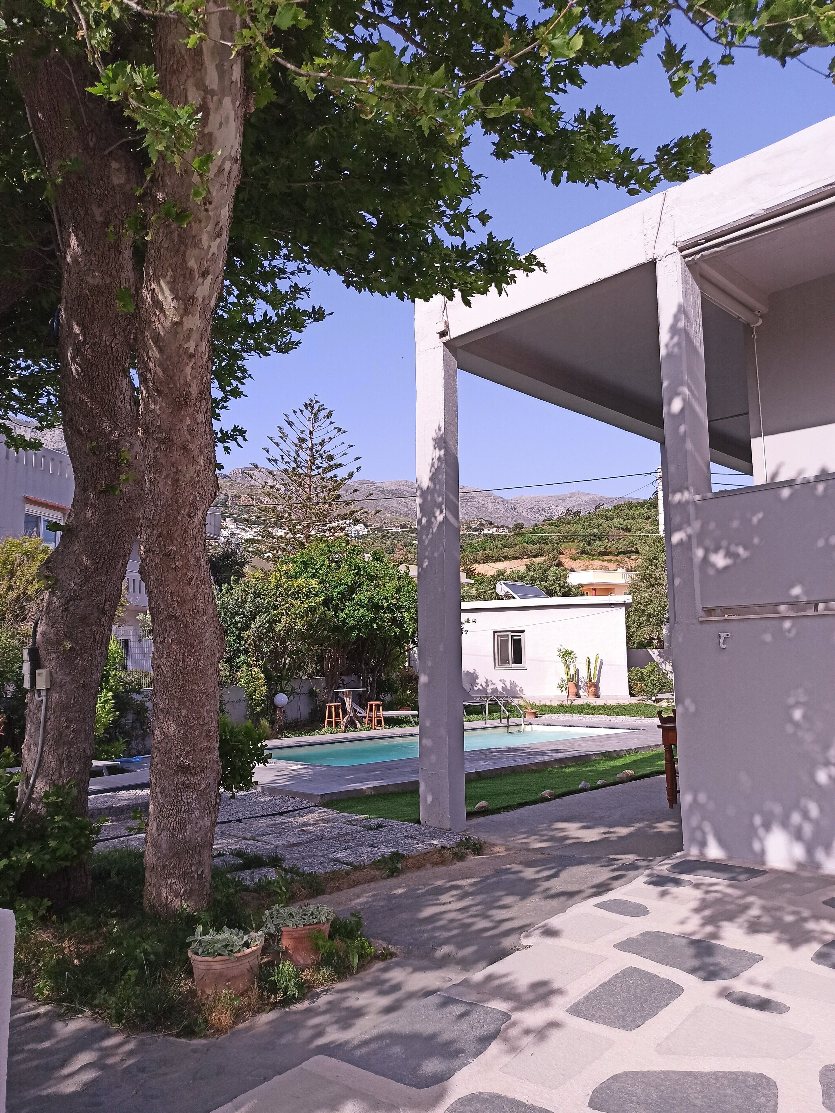 A pool area with a pergola, trees, and a view of a hillside.