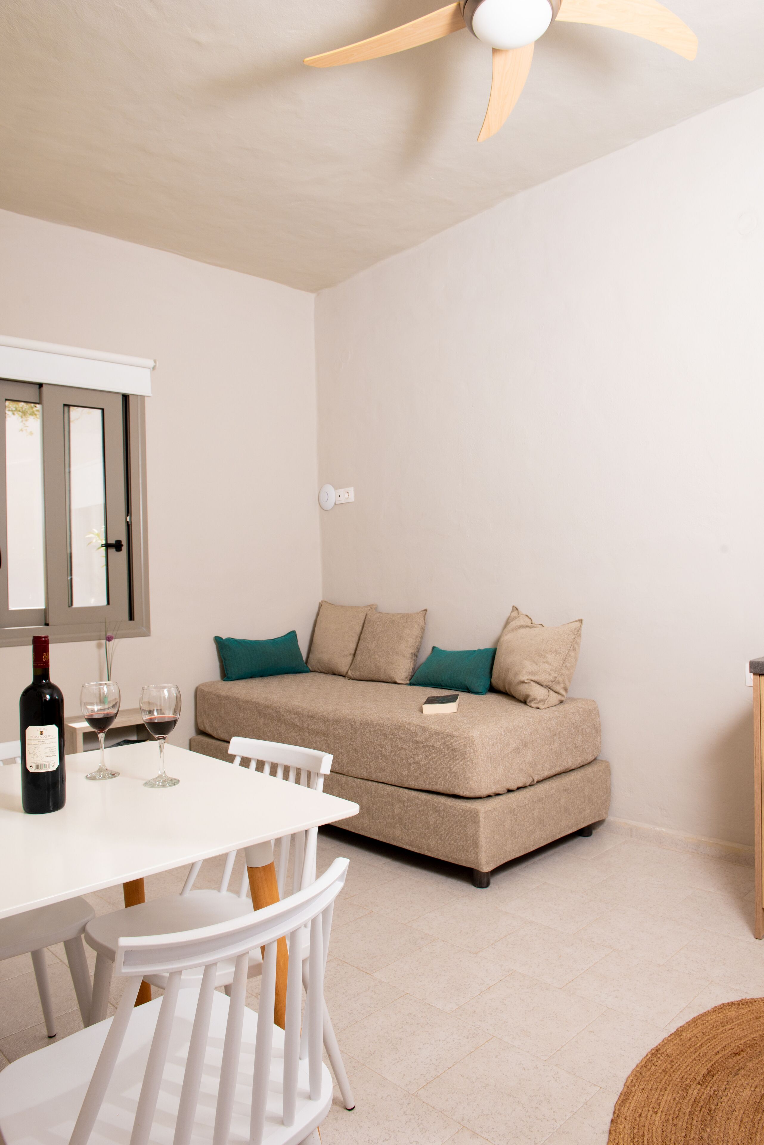 A compact living space with a sofa, a dining table with chairs, a ceiling fan, and a window with blinds.