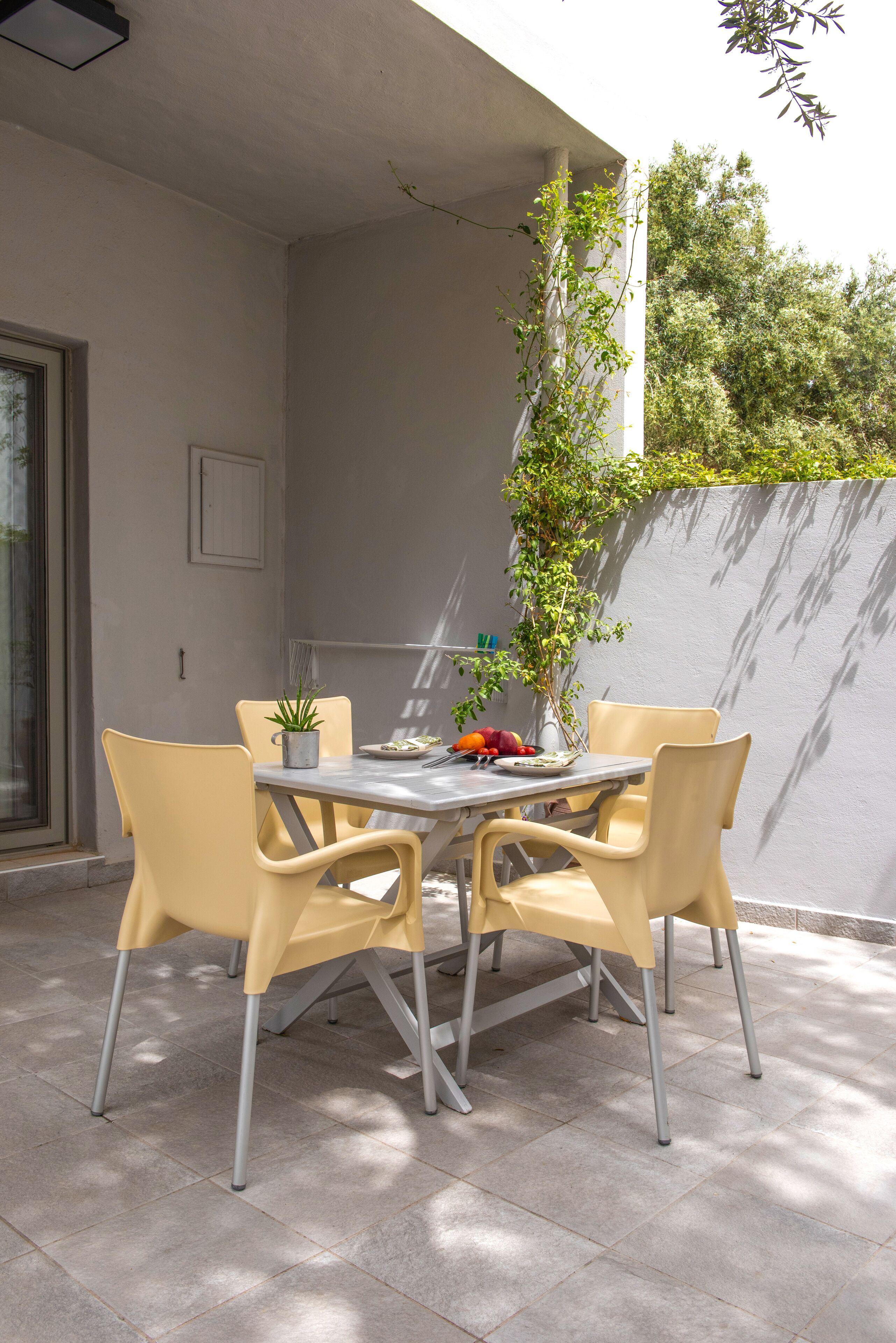 An outdoor patio with a table and four chairs, a potted plant, and a fruit bowl.