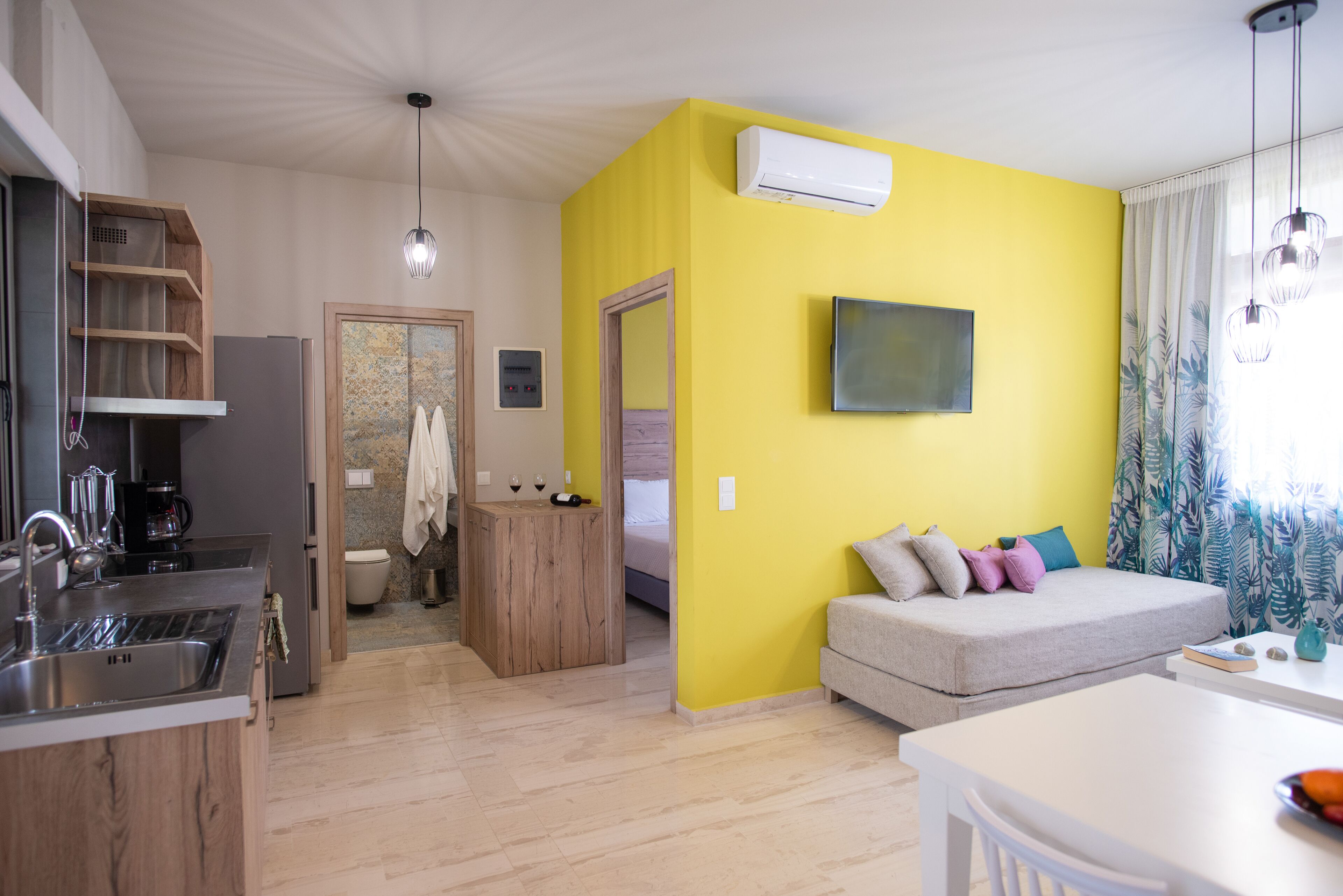A modern apartment with a kitchen, a dining area, and a living room with a sofa and a TV.