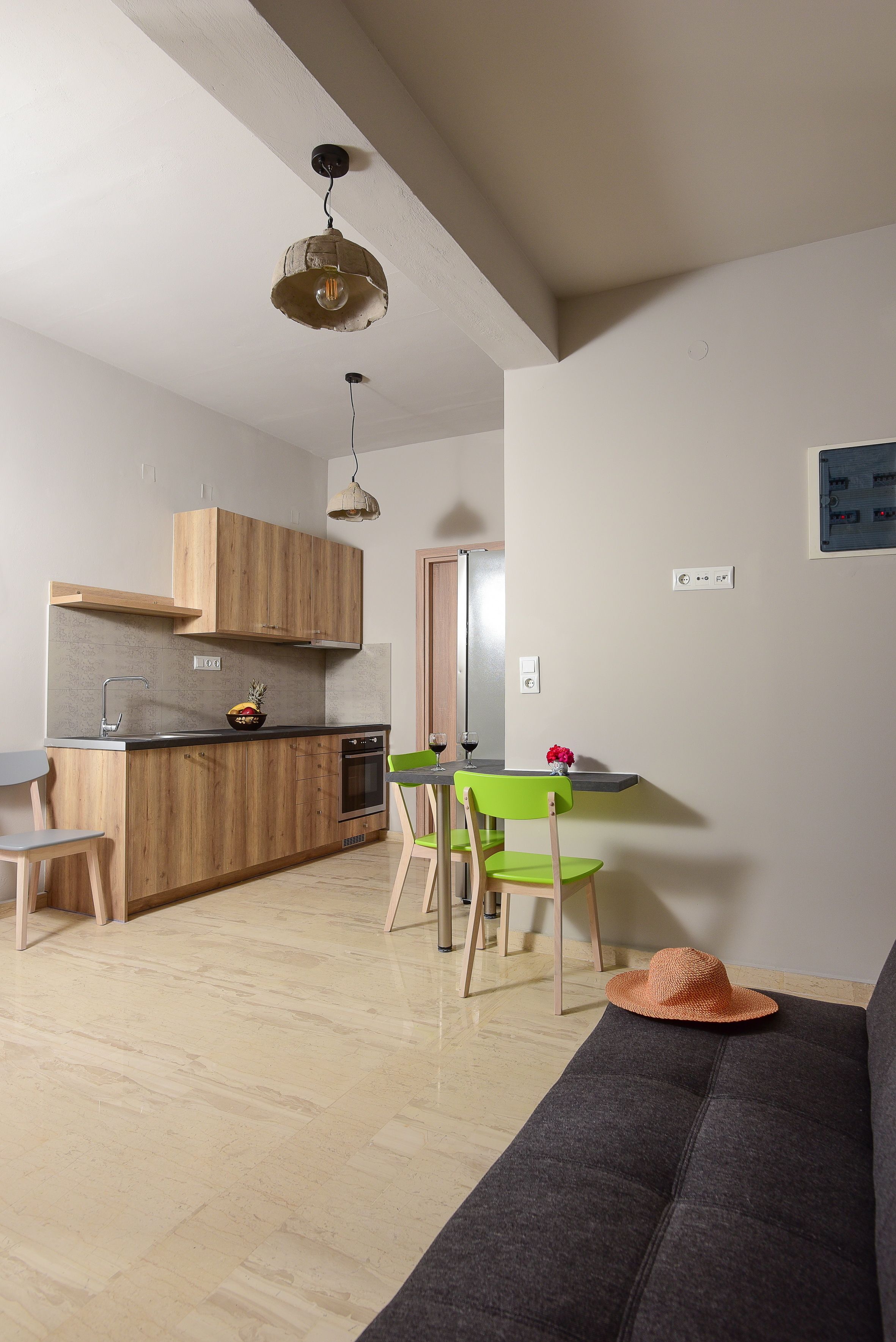 A modern kitchen with wooden cabinets, a dining area with green chairs, and a gray sofa.