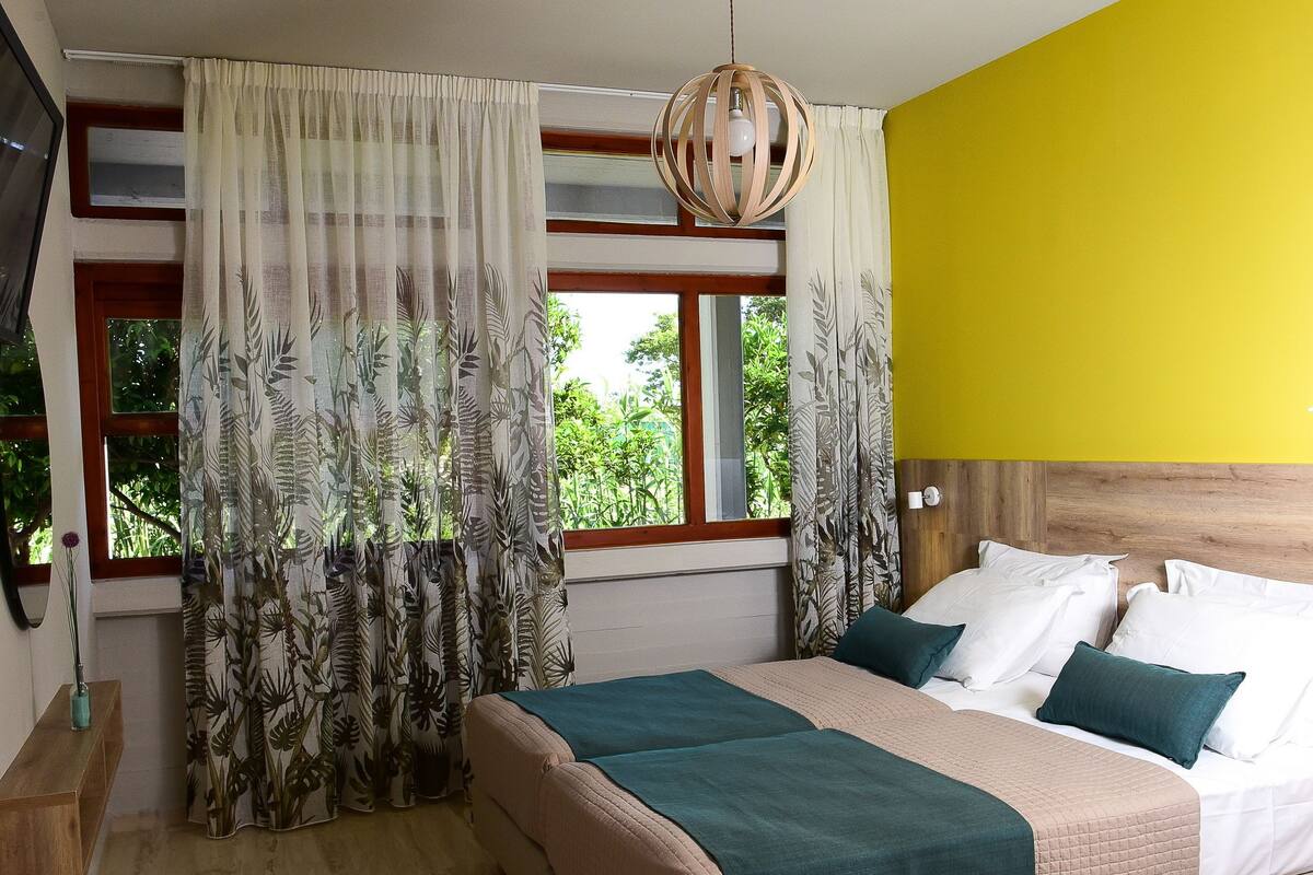 A bedroom with a bed, curtains, a window, and a yellow wall.