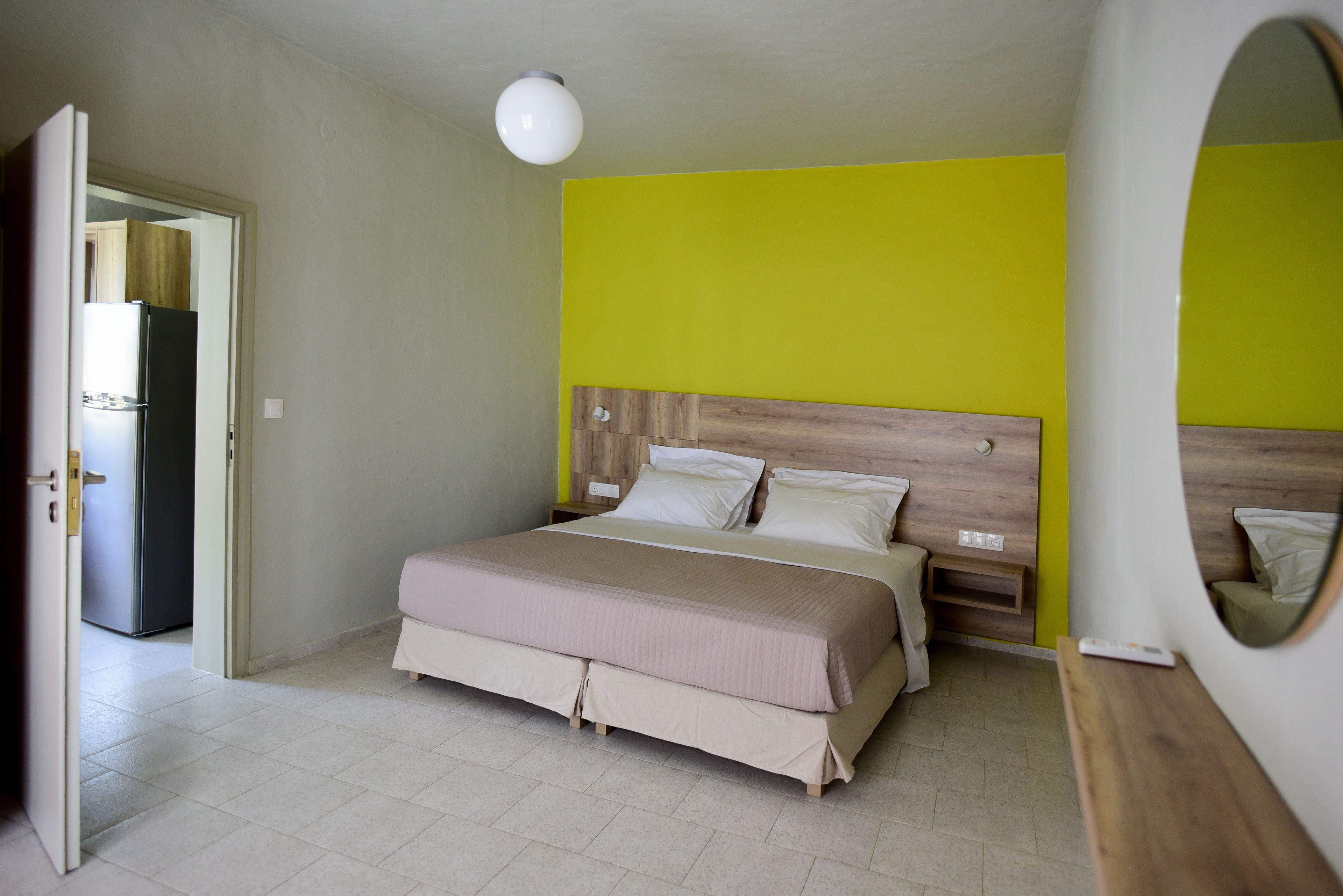 A bedroom with a bed, bedside tables, a mirror, and a door leading to a kitchen.