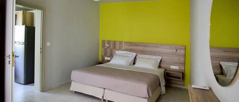 A bedroom with a bed, bedside tables, a mirror, and a door leading to a kitchen.