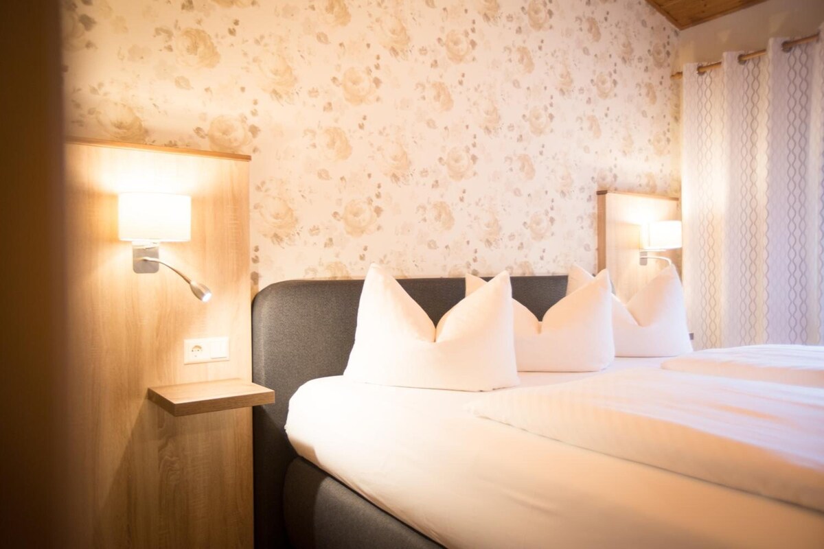 Una habitación de hotel con una cama, dos lámparas de noche y una pared con estampado floral.
