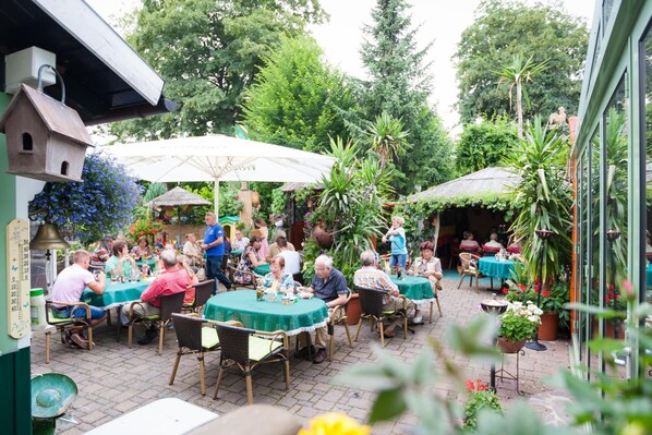 Un área de patio al aire libre con mesas y sillas redondas, rodeada de follaje y plantas en macetas.