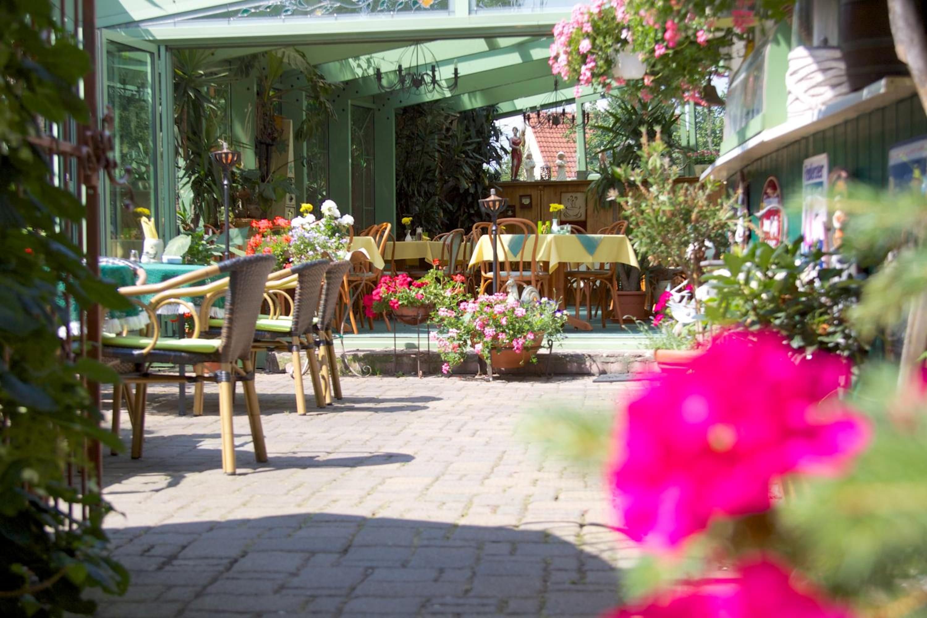 An outdoor seating area with wicker chairs and tables, surrounded by potted plants and flowers.