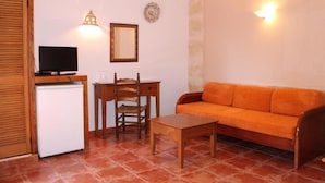 Un espacio habitable pequeño con un refrigerador blanco, un escritorio de madera con una silla, un sofá naranja y un televisor sobre un soporte.