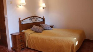 Una cama bien hecha con cabecera de madera, dos lámparas de noche y una mesita de noche de madera con cajones.