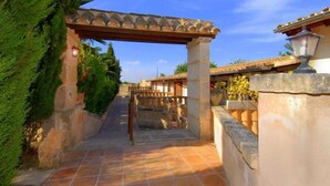Un sendero estrecho que conduce a un edificio con techo de tejas y una estructura de pérgola.