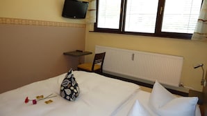Une chambre d’hôtel avec un lit, une petite table, une chaise, un téléviseur fixé au mur et une fenêtre avec des stores.