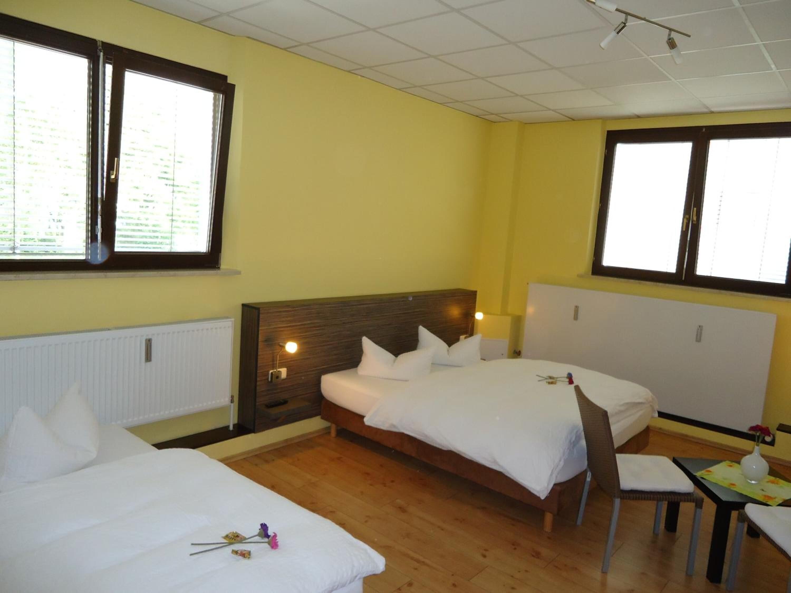 Quarto de hotel com duas camas, piso de madeira e janelas amplas.