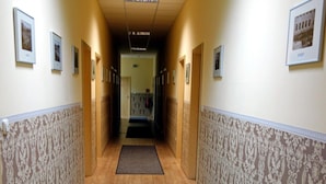 Un couloir avec un papier peint à motifs, un plancher en bois et un tapis bleu qui mène à une porte au fond.