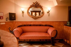 Un canapé de style vintage, doté d’un revêtement à motifs, un miroir décoratif placé au-dessus et des appliques murales.