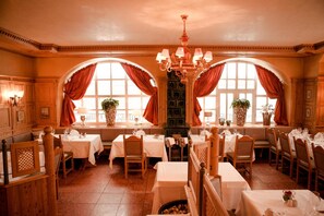 A restaurant with multiple tables and chairs, large windows with curtains, and a chandelier. - Schlosshotel Grunwald (Gruenwald)