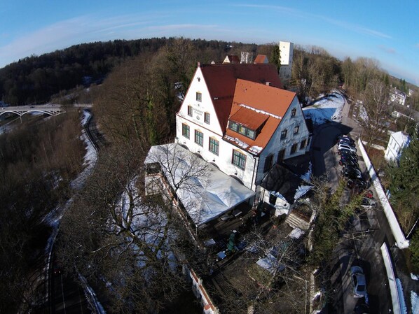 Un grand bâtiment blanc avec un toit rouge, entouré d’arbres et avec un pont en arrière-plan.