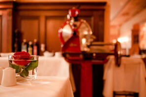 Une table sur laquelle se trouve un verre contenant une rose rouge, des salières et des poivrières, et un objet rouge en arrière-plan.