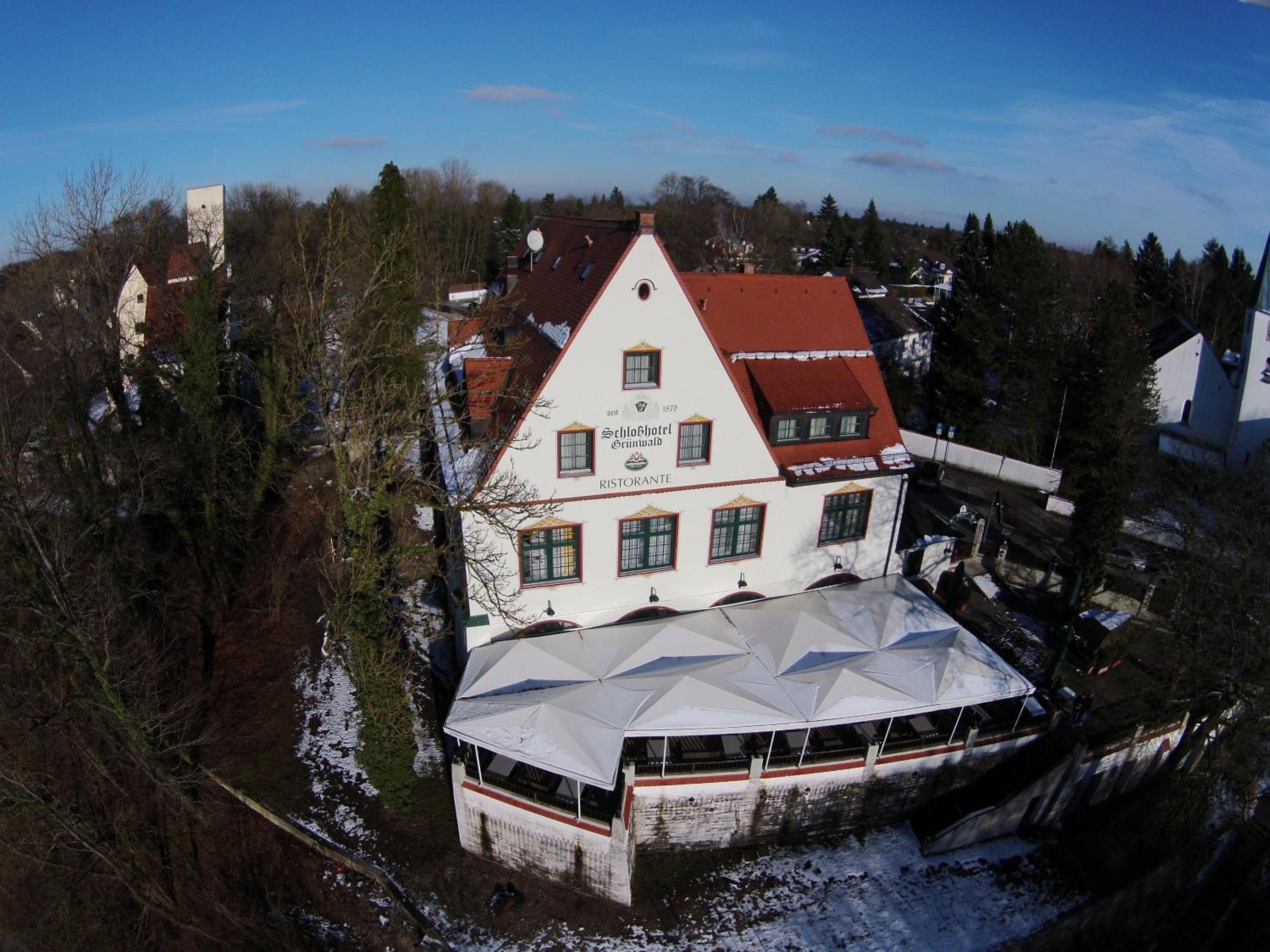 A large building with a prominent white facade and a red roof, surrounded by trees and a body of water.