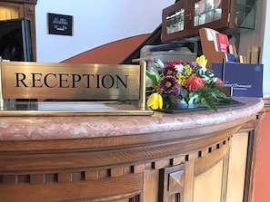 A reception desk with a 'RECEPTION' sign, a floral arrangement, and a blue box with text.