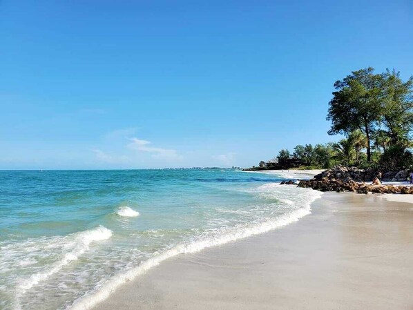 Enjoy serene beach views and tranquil waters, surrounded by lush greenery and a rocky shoreline.