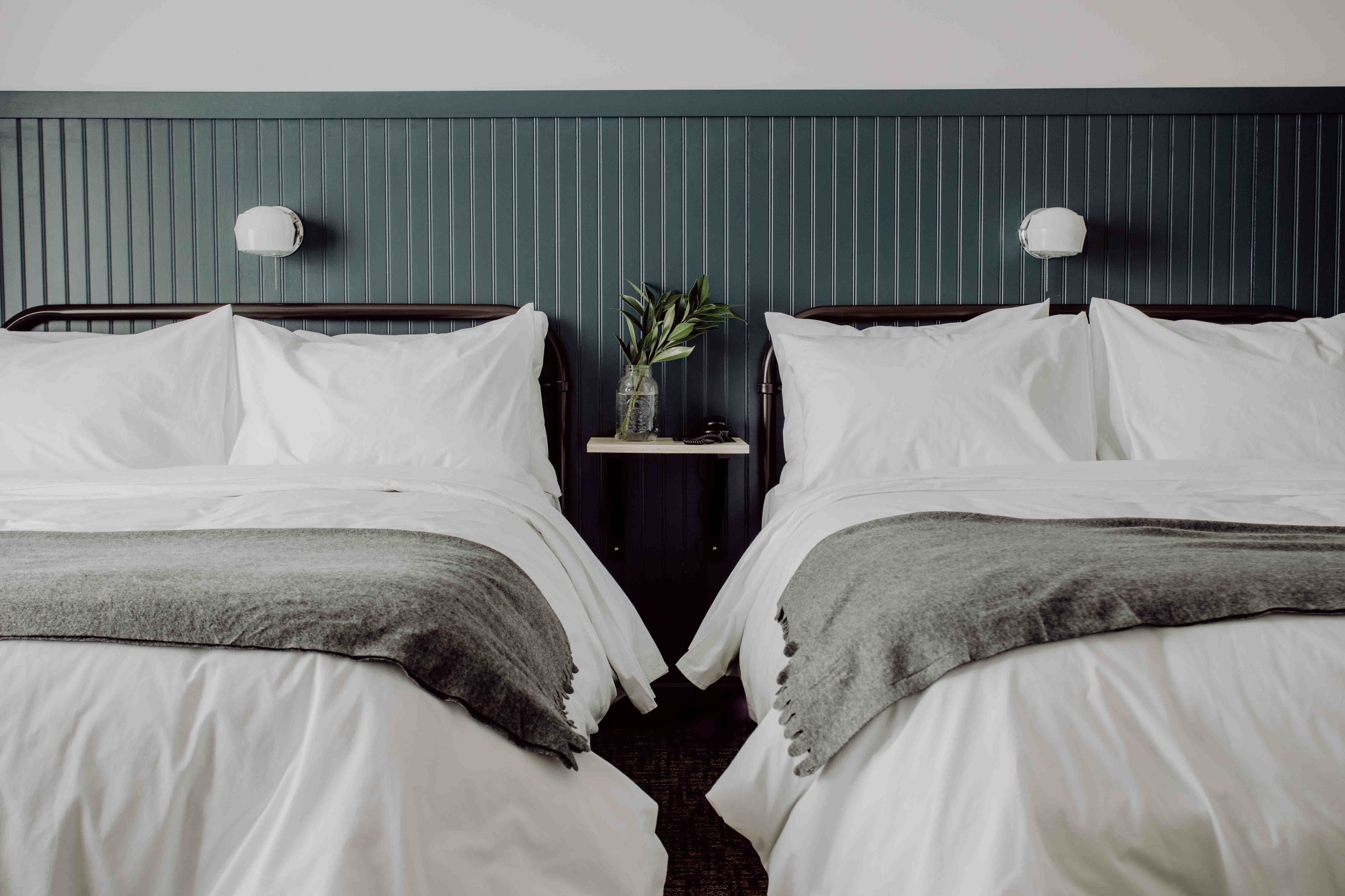 A hotel room with two beds, a nightstand with a vase of flowers, and wall-mounted lamps.