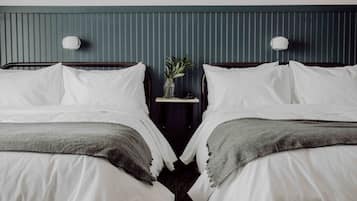 A hotel room with two beds, a nightstand with a vase of flowers, and wall-mounted lamps.