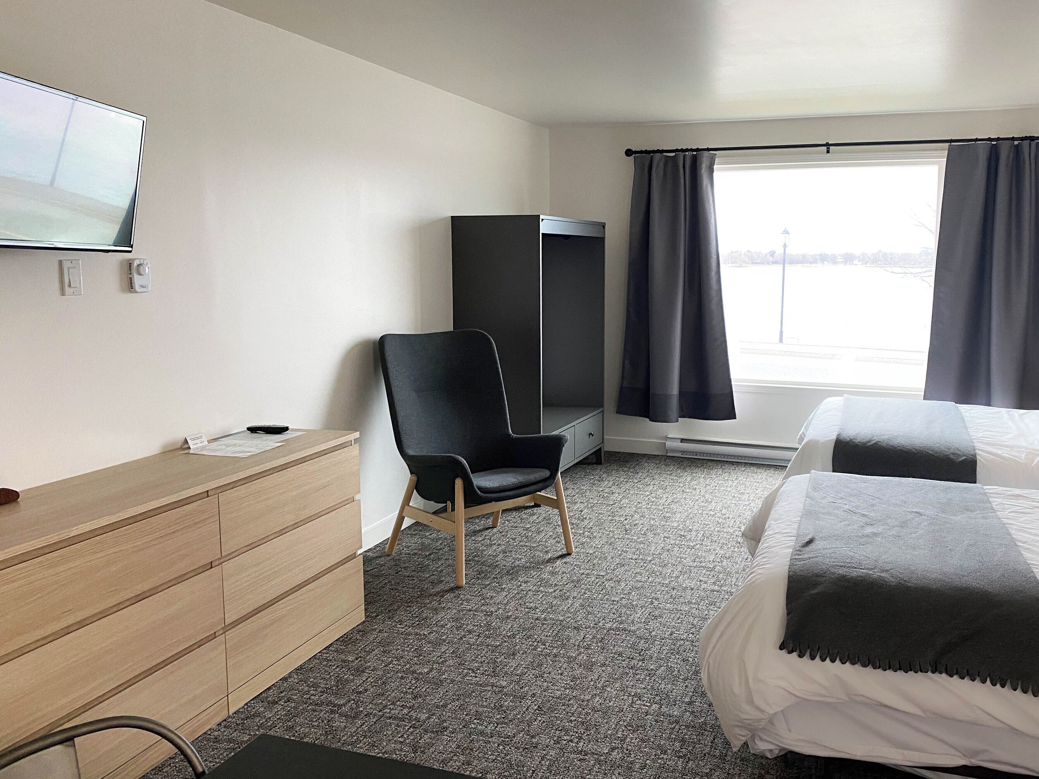 Habitación de hotel con cama, escritorio, silla, armario, televisor y ventana con cortinas.