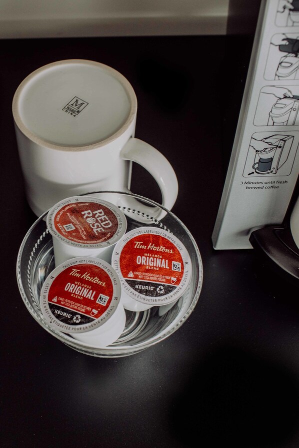 Una taza blanca con un logo, una bandeja con tres cápsulas de café y el manual de la máquina de café.