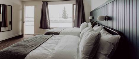 A hotel room with two beds, a large window with curtains, a wooden headboard, and a mirror on the wall.