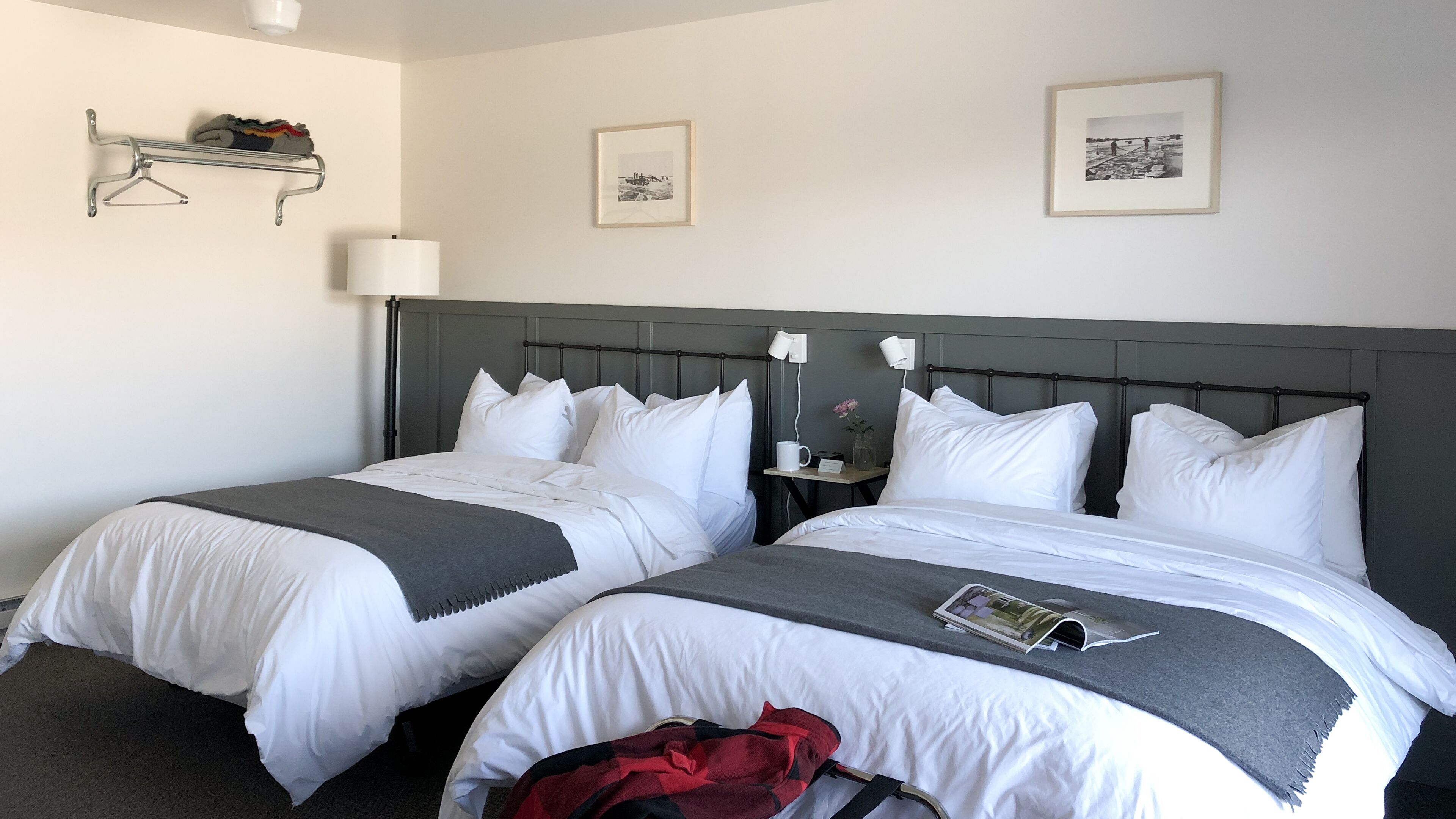 A hotel room with two beds, a bedside table with a lamp, and a small shelf with a decorative item.