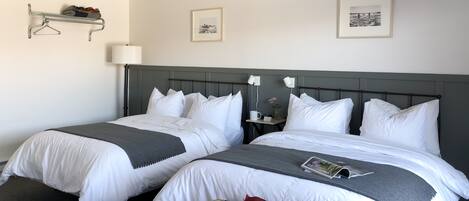 A hotel room with two beds, a bedside table with a lamp, and a small shelf with a decorative item.