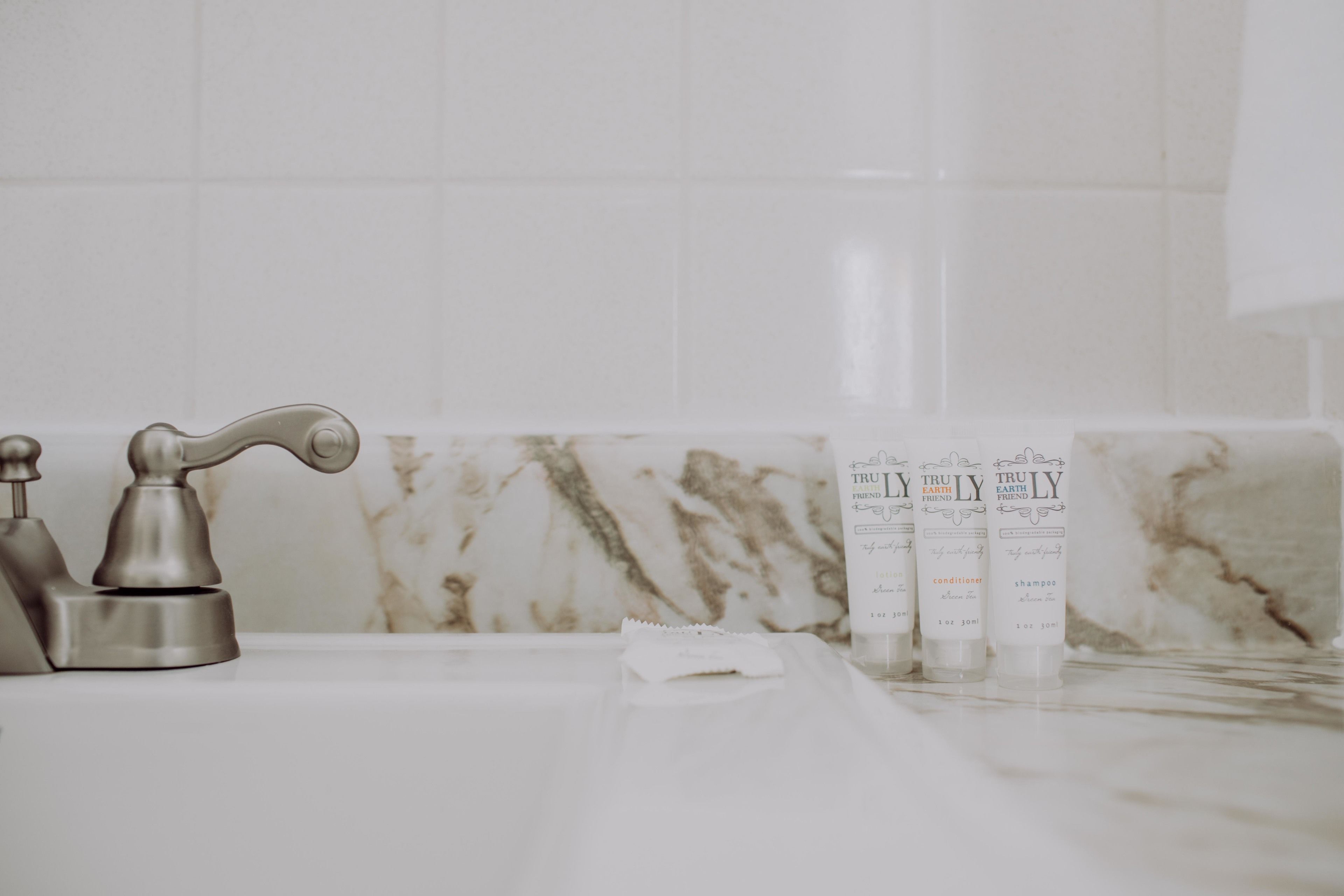 A bathroom with a marble sink, a faucet, and three bottles of shampoo and conditioner.